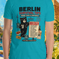 Person wearing a blue t-shirt with 'Berlin Survival Tips' design, surrounded by scenic and tropical elements.