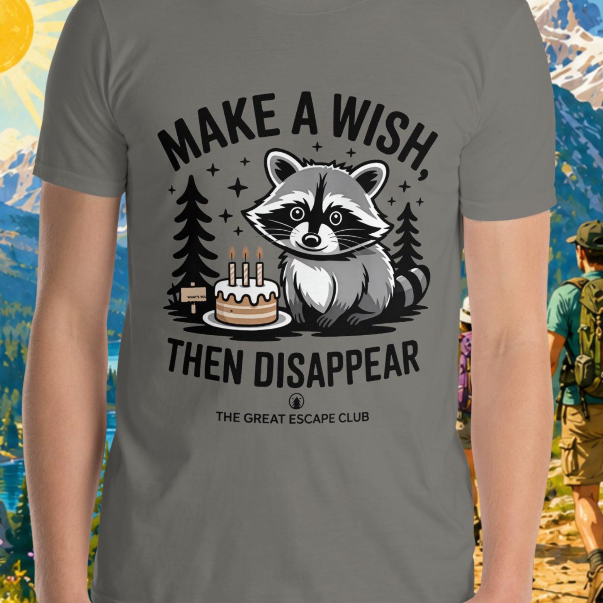 Person wearing a t-shirt with a raccoon graphic and text in front of a scenic mountain backdrop