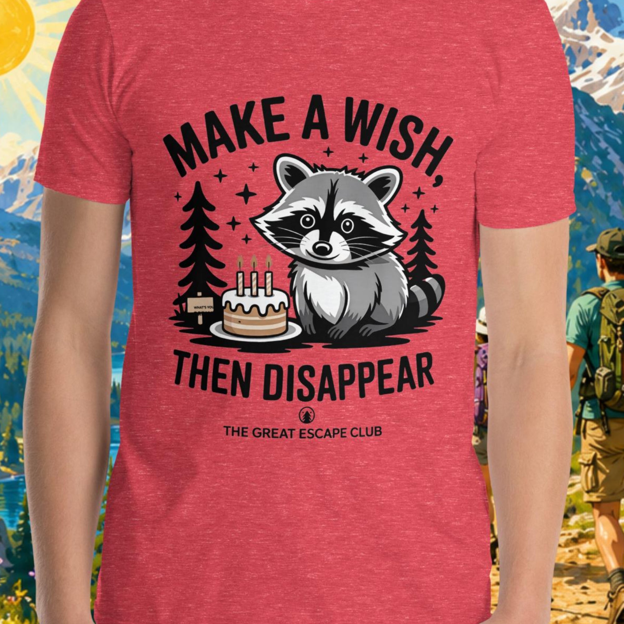 Person wearing a red t-shirt with a raccoon graphic and text, standing in front of a scenic mountain landscape.