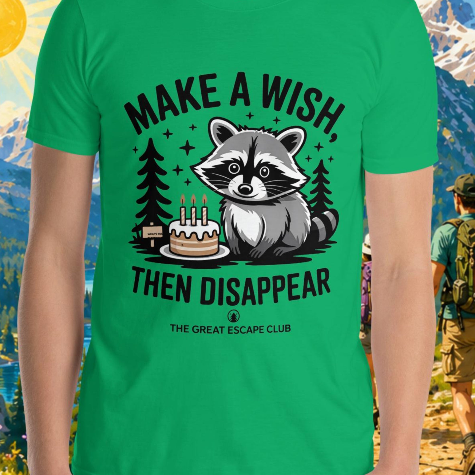 Person wearing a green t-shirt with a raccoon graphic and text in front of a scenic mountain backdrop.