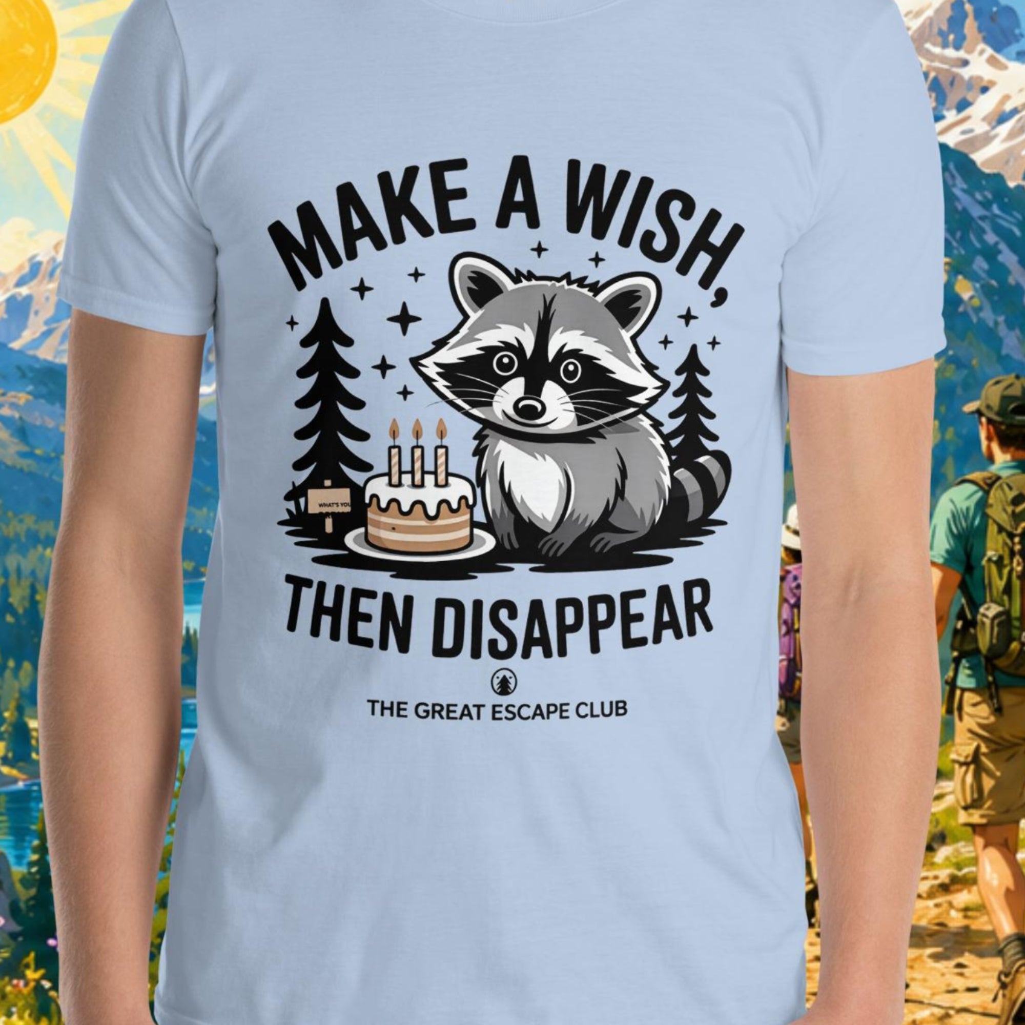 Person wearing a t-shirt with a raccoon graphic and text in front of a scenic mountain backdrop.