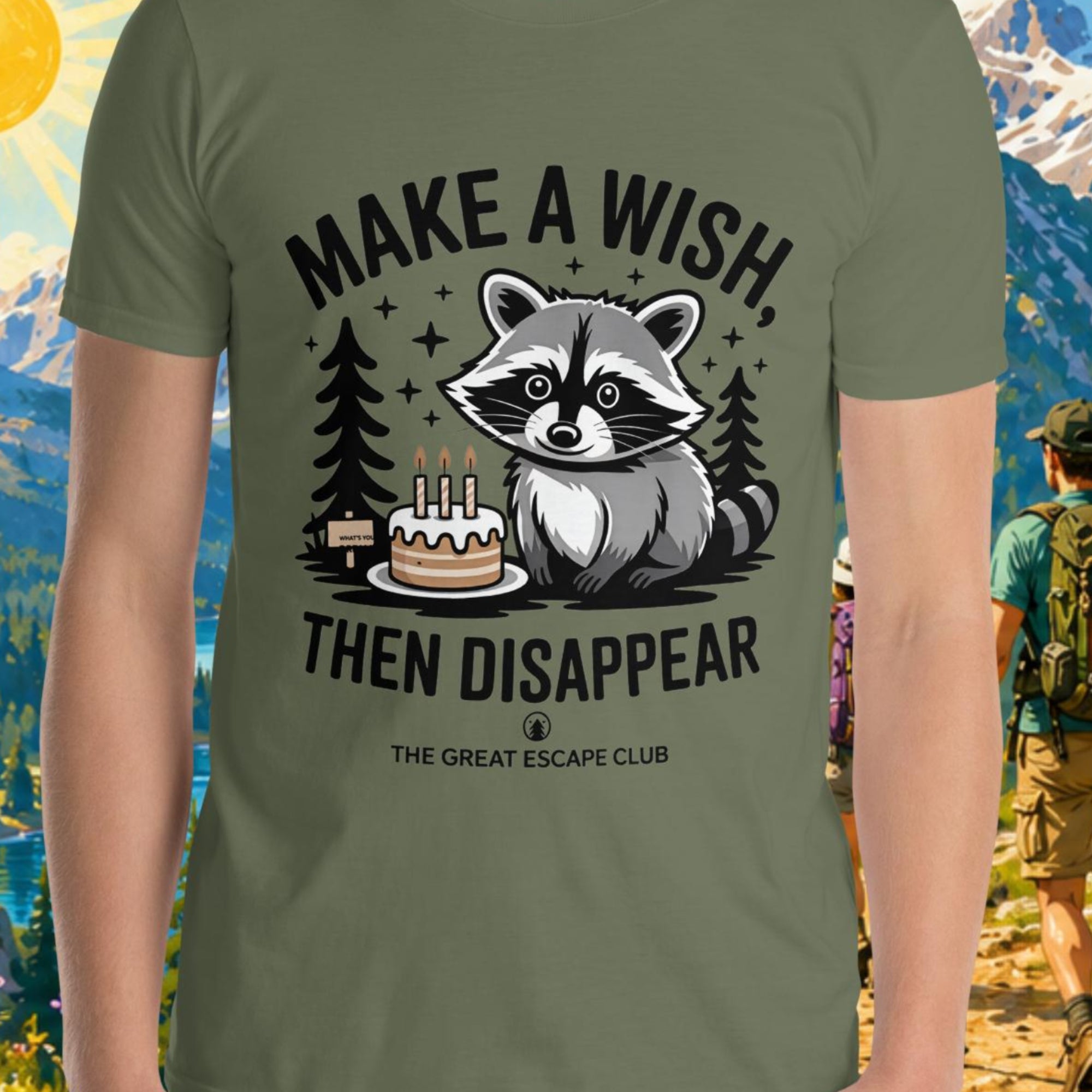 Person wearing a green t-shirt with a raccoon graphic and text, standing in front of a scenic mountain backdrop.