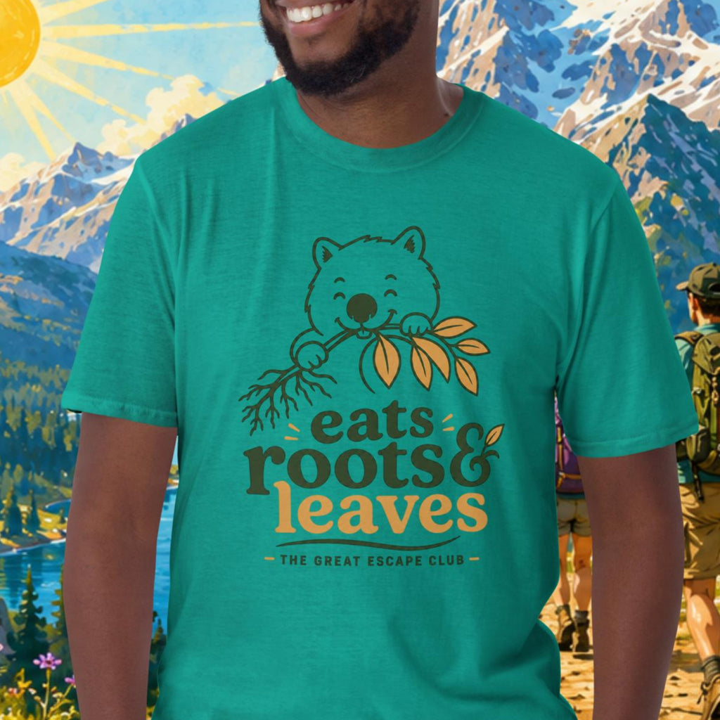 Man wearing a teal t-shirt with 'eats roots & leaves' design in a mountainous landscape.