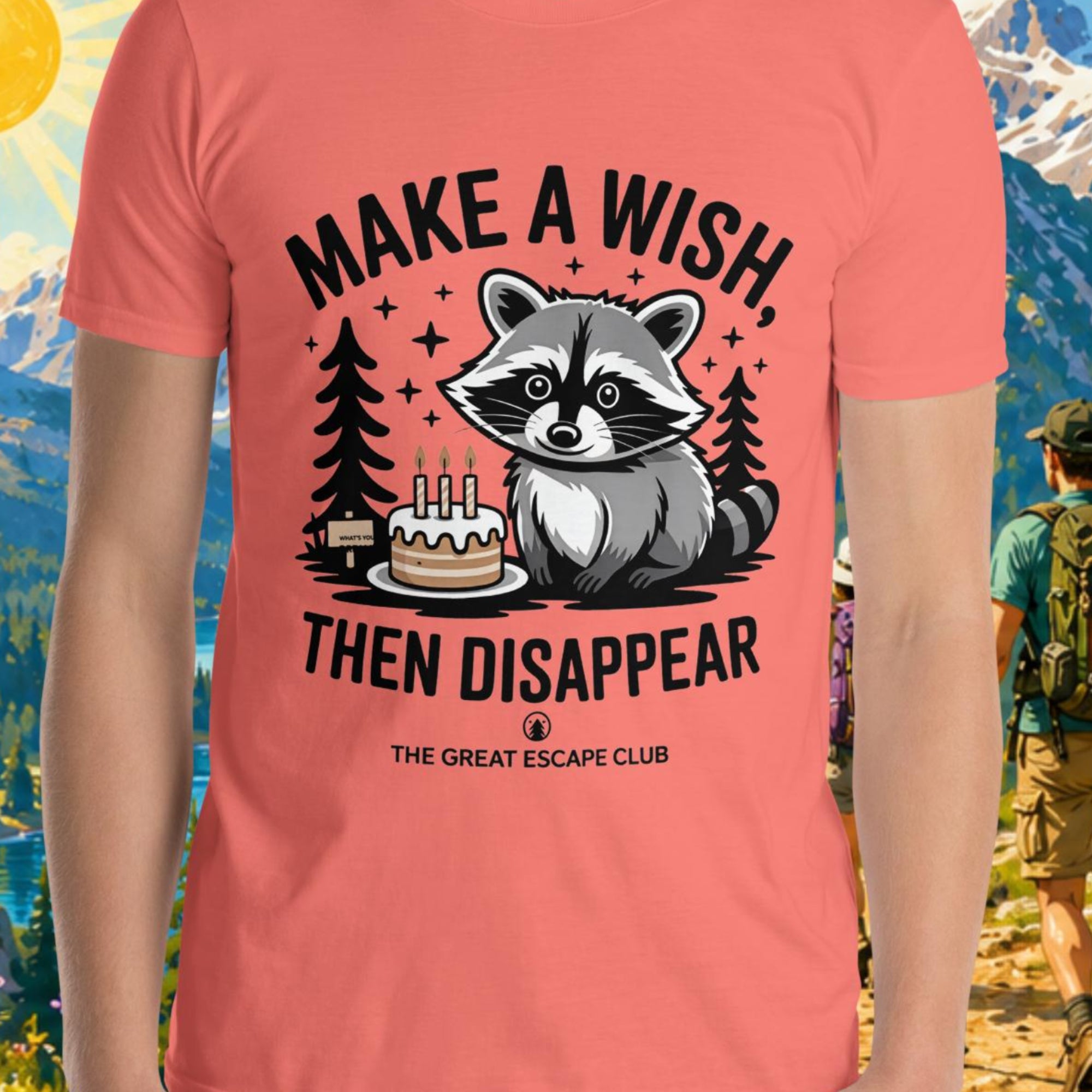 Person wearing a pink t-shirt with a raccoon graphic and text, standing in front of a scenic mountain landscape.