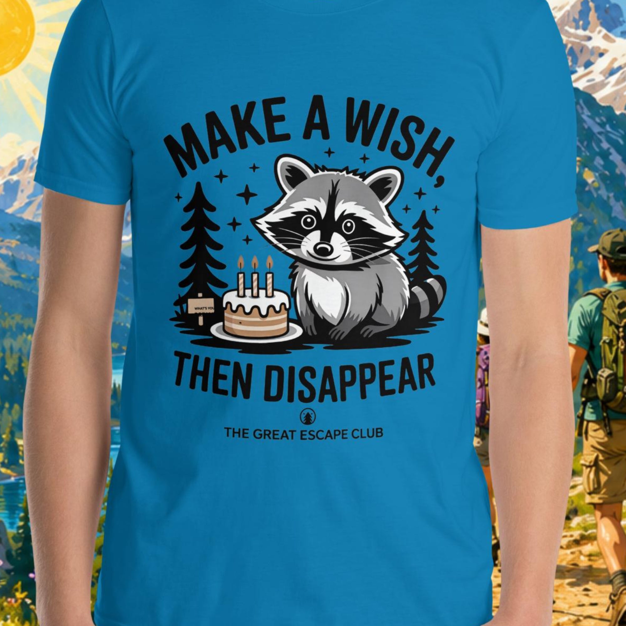 Person wearing a blue t-shirt with a raccoon graphic and text in front of a scenic mountain backdrop.