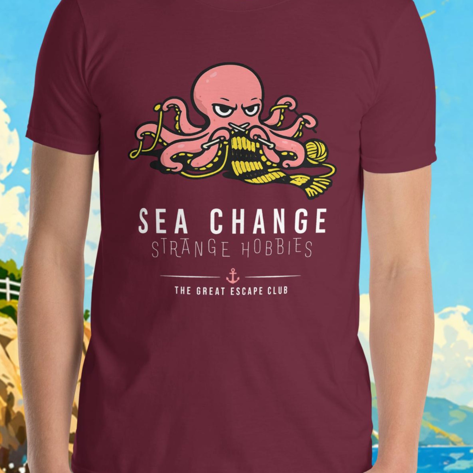 Person wearing a maroon t-shirt with an octopus design and text, standing in front of a scenic background with a lighthouse and sailboat.