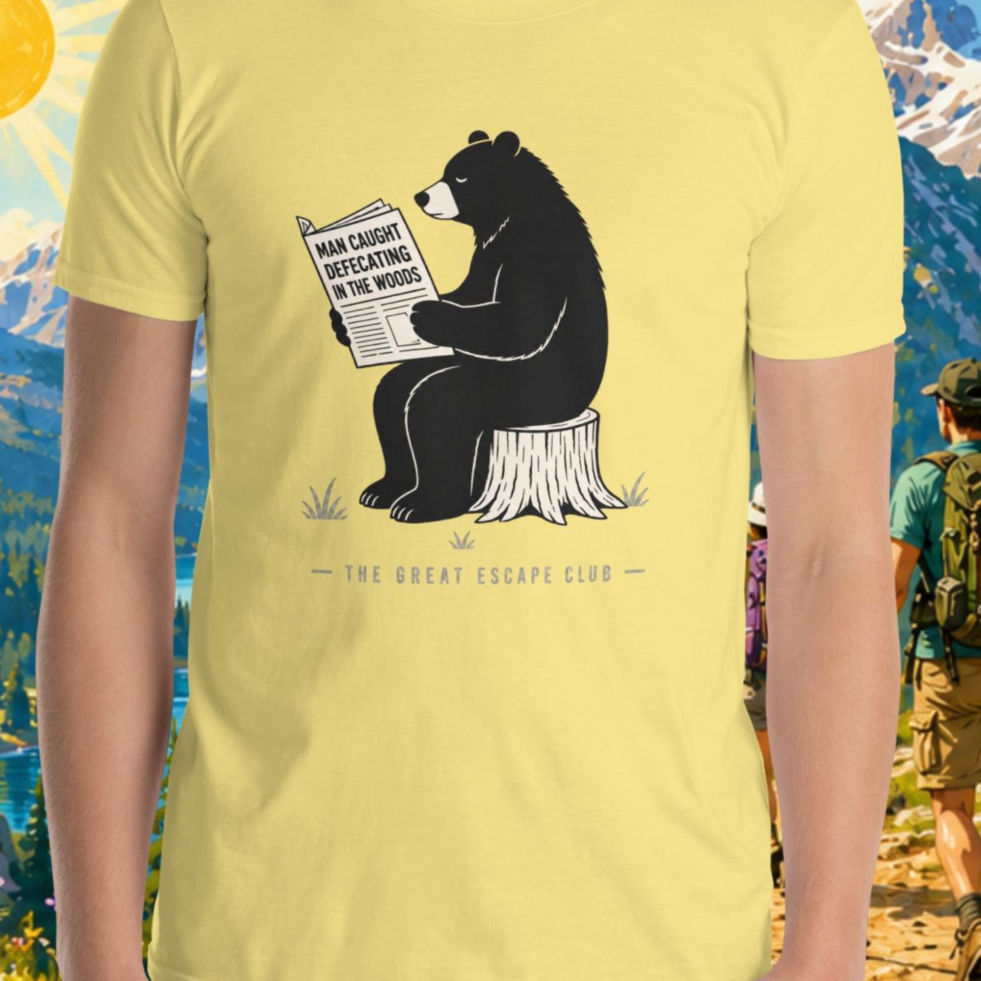 Yellow t-shirt with a bear graphic reading a newspaper, set against a scenic outdoor background.
